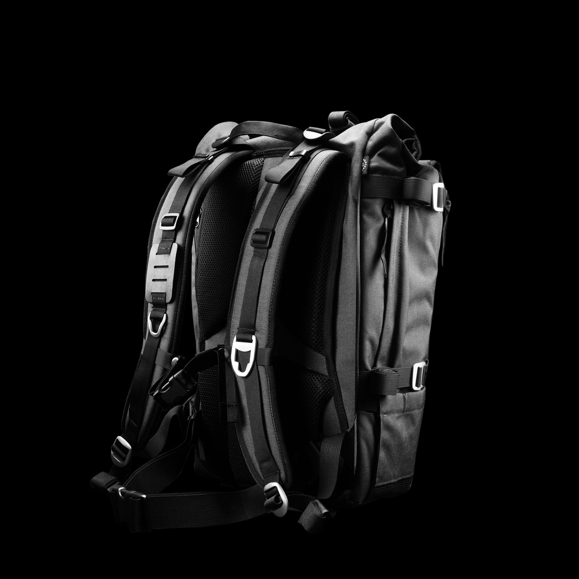 The Peloton Asphalt S expandable roll-top backpack, three-quarter back view on pure black — LBB flagship in collaboration with Thrive Motorcycle.