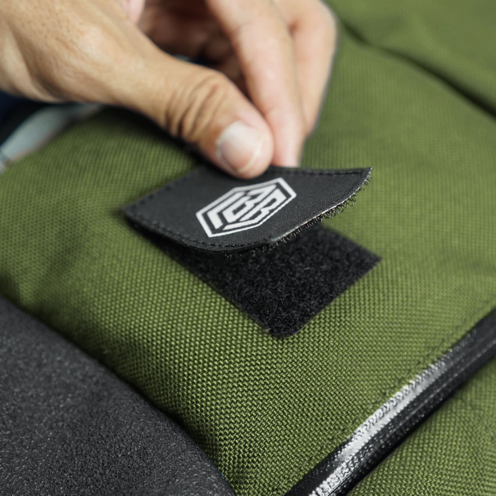 Macro of the hexagonal LBB monogram patch on olive canvas of The Peloton backpack.